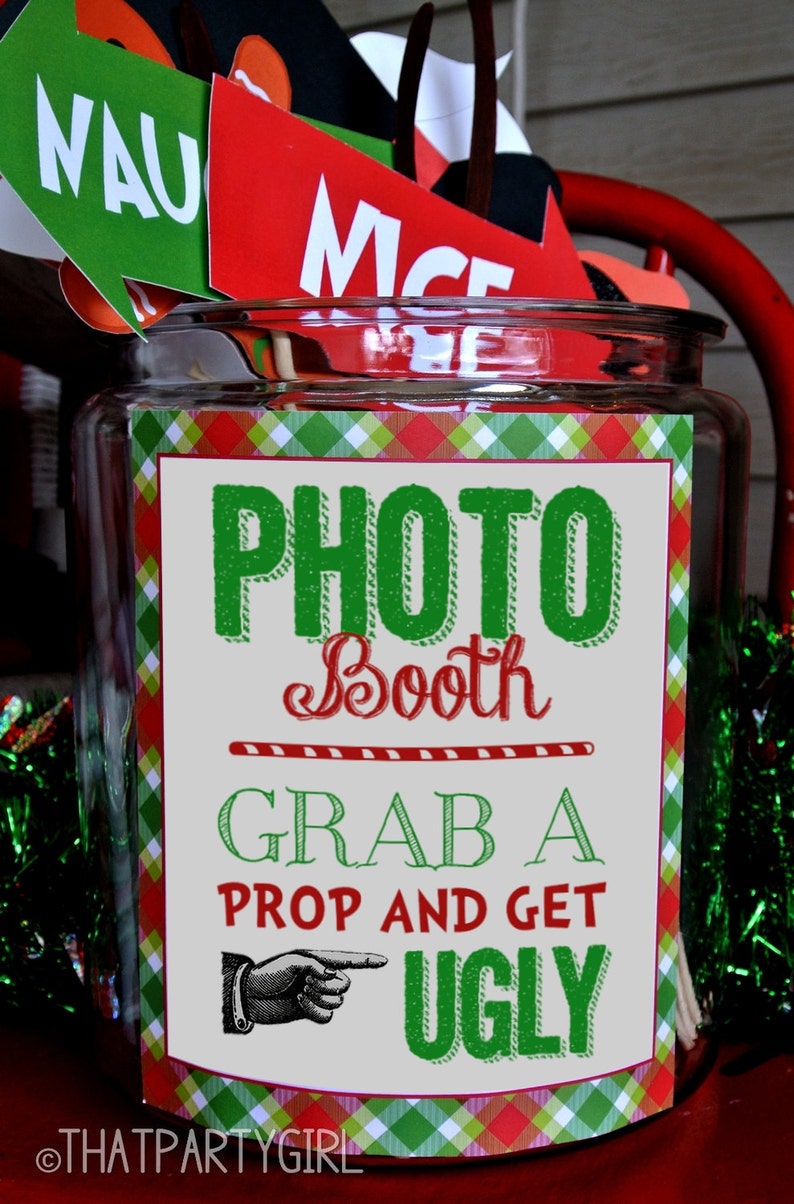 May include: A clear glass jar with a red and green plaid label that says "Photo Booth Grab a Prop and Get Ugly". The jar is filled with various props for a photo booth, including a green and white sign that says "NAUGHTY" and a red sign that says "NICE".