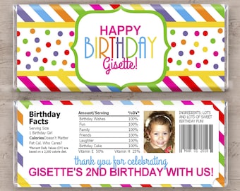 Puede incluir: Un envoltorio de barra de chocolate colorido con un fondo rayado arcoíris y lunares. El envoltorio dice "¡Feliz cumpleaños Gisette!" y "¡El 2º cumpleaños de Gisette con nosotros!" También incluye una foto de una niña y una etiqueta de información nutricional.