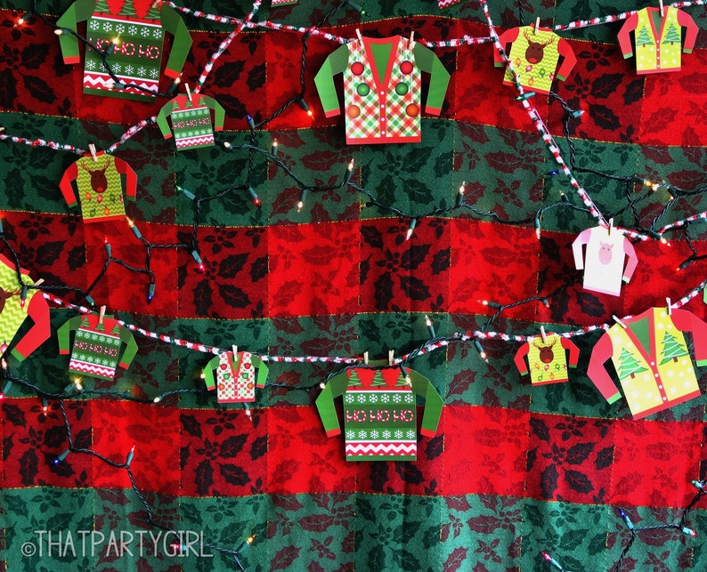 May include: A string of festive Christmas lights with paper cutouts of Christmas jumpers hanging from them. The jumpers are decorated with various holiday patterns, including snowflakes, reindeer, and the phrase "Ho Ho Ho".