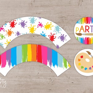 May include: Set of cupcake wrappers and toppers with a paint splatter and rainbow brushstroke design. The toppers feature a paintbrush and palette and the text "PARTY!"