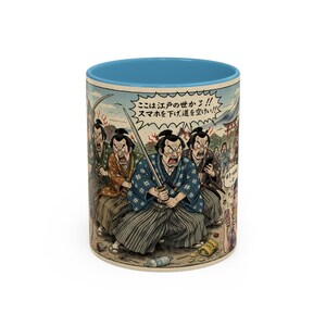 Puede incluir: Taza de cerámica con interior azul. El exterior presenta una ilustración de estilo cómic de figuras de samuráis, algunos sosteniendo espadas, con texto japonés. El fondo es azul claro con una escena de montaña y cielo.
