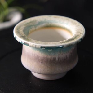 May include: A white ceramic mug with a black handle and the text "But First, Coffee" in a bold, black font. The mug is set against a neutral background, highlighting its simple design.
