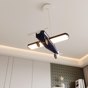 May include: A navy blue airplane-shaped ceiling light with white propeller and wing lights. The light is suspended from the ceiling by a thin white cord. The fixture has a classic airplane design, suitable for a child's room.