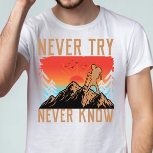May include: White t-shirt with a graphic design featuring a hiker on a mountain, a sunset, and the text "NEVER TRY NEVER KNOW" in gold. The design includes trees and birds, creating a nature-themed aesthetic.