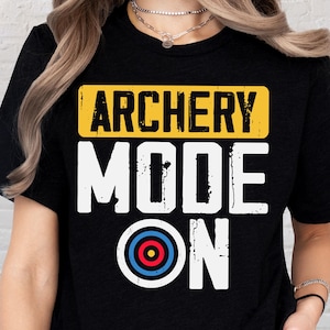 May include: Black t-shirt with the text "ARCHERY MODE ON" in white, yellow, and blue. The design includes a yellow rectangle with "ARCHERY" in black, and a target graphic. The shirt is a casual wear item.