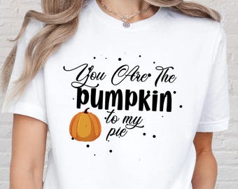 May include: White t-shirt with the text "You Are The Pumpkin to my pie" in black script and a cartoon pumpkin graphic. The shirt is a short-sleeved crew neck.