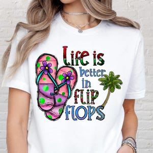 May include: White t-shirt featuring a colorful graphic of two flip-flops with purple flowers and green polka dots. The text "Life is better in flip flops" is also displayed, along with a palm tree.