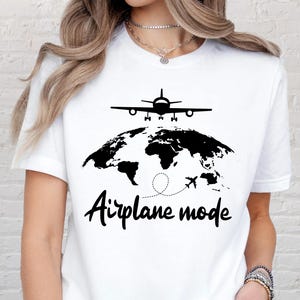 May include: White t-shirt with a black graphic of an airplane above a world map and the words "Airplane mode" in a handwritten font. The design features a dotted line and a small airplane.