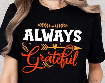 May include: Black t-shirt with the words "ALWAYS Grateful" in white and orange script. The design includes decorative arrows and leaf accents, creating a fall-themed graphic.