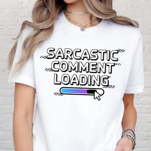 Peut inclure: T-shirt blanc avec l'inscription "SARCASTIC COMMENT LOADING" en noir, accompagnée d'une barre de chargement bleue et violette et d'un curseur blanc. Le t-shirt est à col rond et à manches courtes.