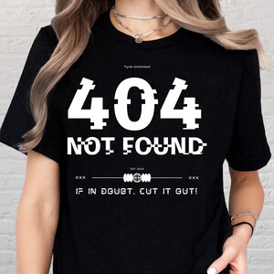May include: Black t-shirt with the text "404 NOT FOUND" in white, pixelated font. The shirt also features the text "IF IN DOUBT, CUT IT OUT!" and the brand name "Tynk Unlimited".