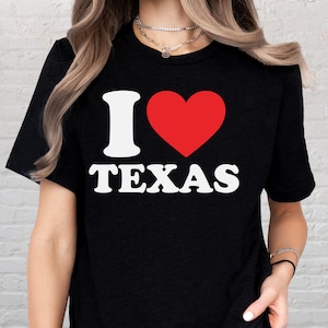 May include: Black t-shirt with the text "I ❤️ TEXAS" in white and red. The "I" is white, the heart is red, and the word "TEXAS" is in a bold, sans-serif font.