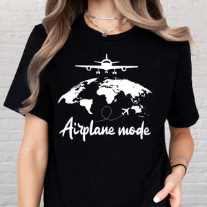 May include: Black t-shirt with a white graphic of an airplane above a world map. The text "Airplane mode" is written in a cursive font below the map. The design is simple and clean, perfect for travel enthusiasts.