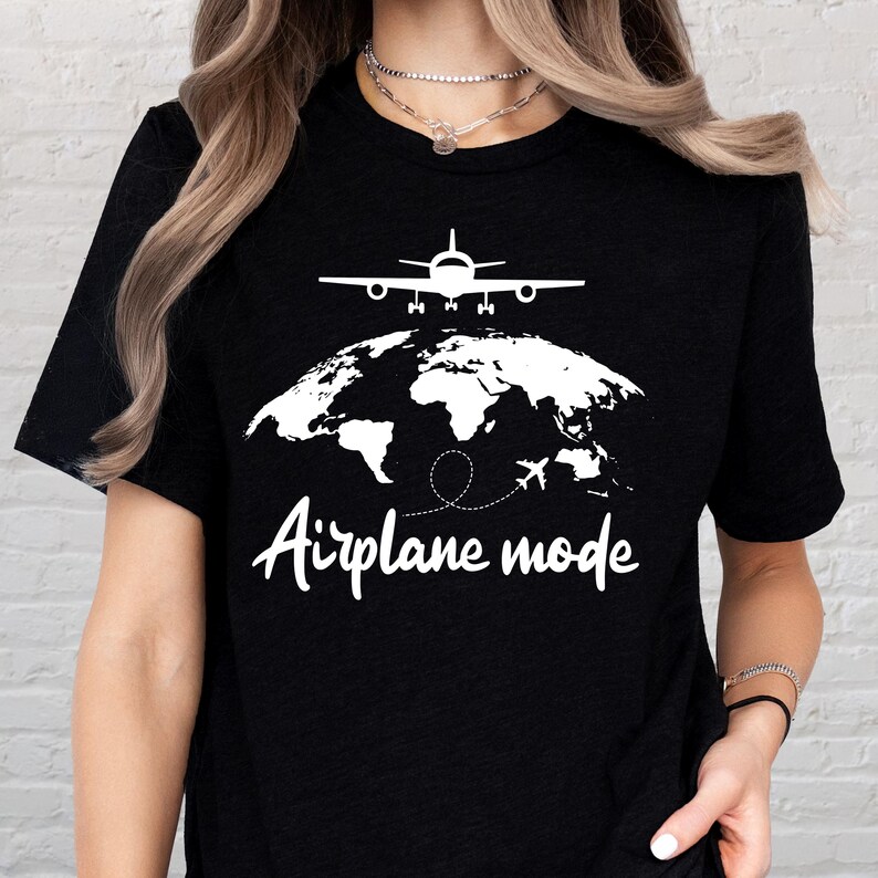 May include: Black t-shirt with a white graphic of an airplane above a world map. The text "Airplane mode" is written in a cursive font below the map. The design is simple and clean, perfect for travel enthusiasts.