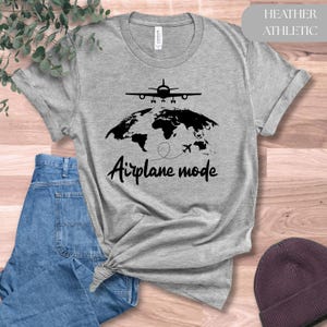 May include: Heather athletic gray t-shirt with a black graphic of an airplane above a world map and the words "Airplane mode". The shirt is made of a soft material and has a crew neck.
