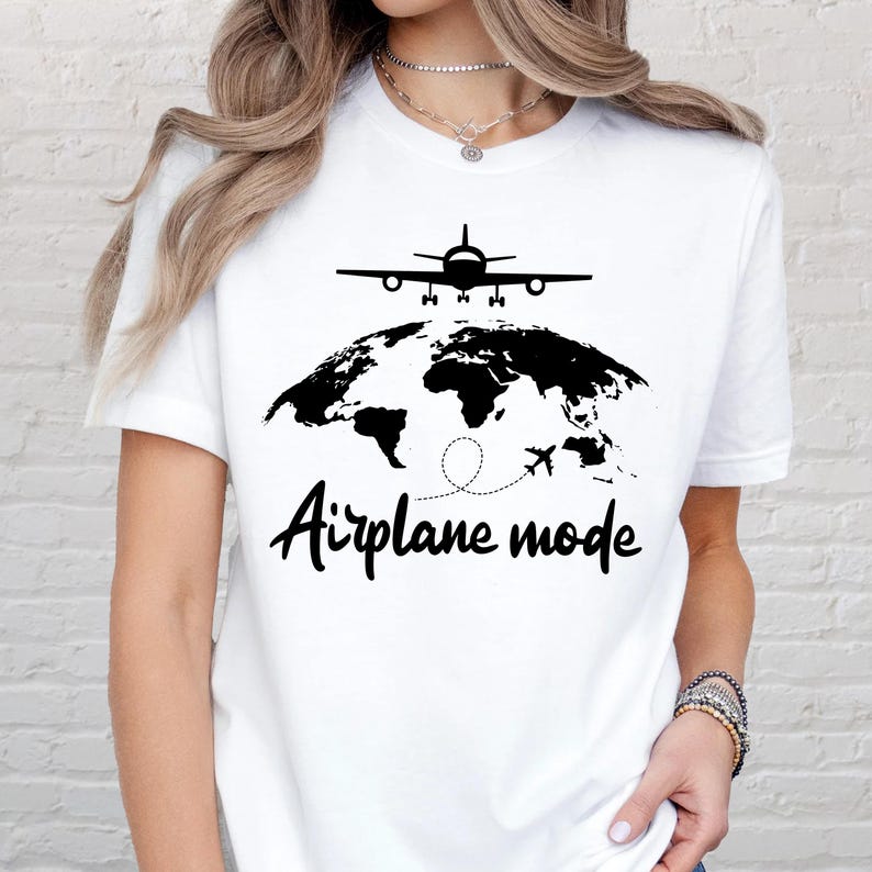 May include: White t-shirt with a black graphic of an airplane above a world map and the words "Airplane mode" in a handwritten font. The design features a dotted line and a small airplane.