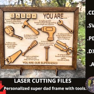 May include: Wooden framed sign with the word "DADDY" in Scrabble tiles and various tool cutouts. The sign includes text describing a father's qualities, such as being "as smart as a tape measure." The phrase "YOU ARE OUR SUPERHERO!" is at the bottom.