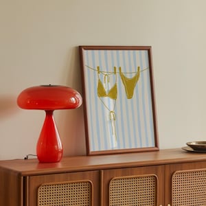 May include: A wooden cabinet with four doors, each featuring a woven rattan panel. A red mushroom-shaped lamp sits on top, next to a framed print of a bikini. A small, dark plate rests on the cabinet's surface. The cabinet is 150 cm long.