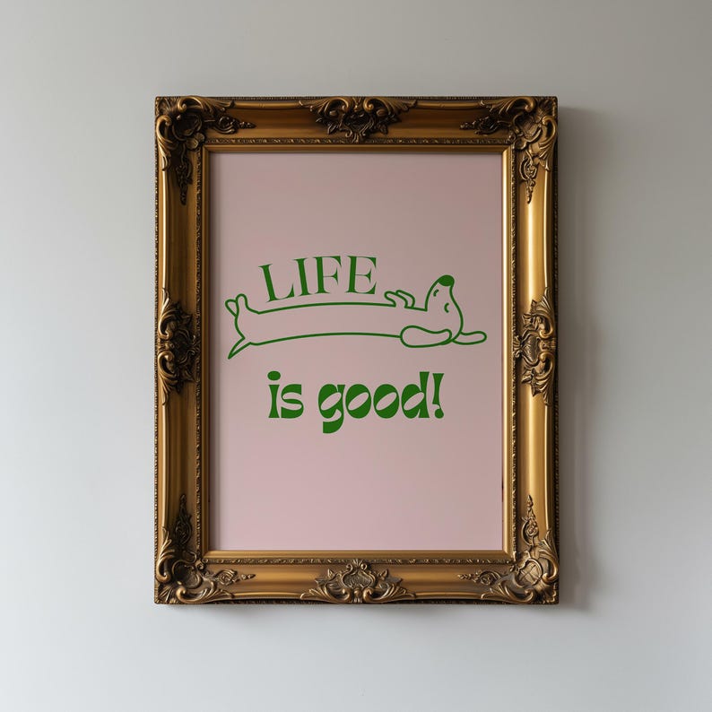 Peut inclure: Une affiche encadr&eacute;e dans un cadre dor&eacute; orn&eacute;. L'affiche a un fond rose clair avec du texte vert et une illustration de teckel. Le texte dit "LIFE is good!"