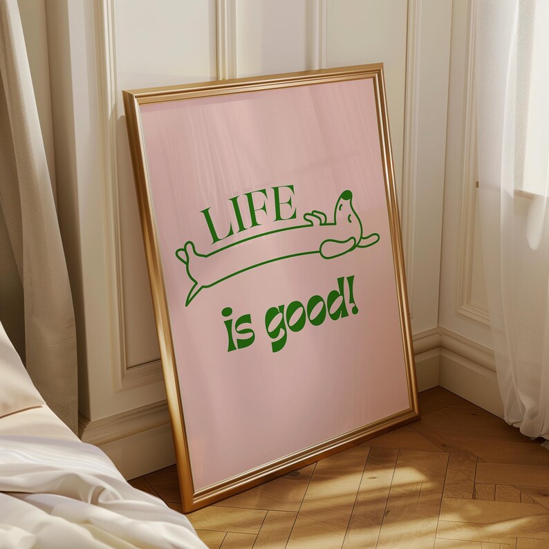 Peut inclure: Affiche rose encadr&eacute;e avec l'inscription verte &laquo; LIFE is good! &raquo; et une illustration de teckel vert. Le cadre dor&eacute; est pos&eacute; contre un mur blanc. Il s'agit d'un objet d&eacute;coratif.