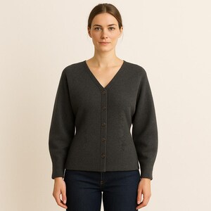 May include: A dark gray cardigan with a V-neck and button-up front. The long sleeves have a slight puff at the shoulder. The cardigan is made of a soft material and is paired with dark blue jeans.
