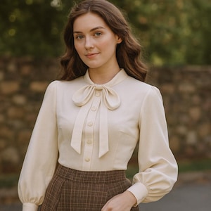 Pode incluir: Blusa creme com gola de laço e mangas compridas. A blusa tem uma frente abotoada e é combinada com uma saia xadrez castanha. O estilo é clássico e elegante, adequado para uma estética vintage ou retro.