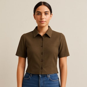 Puede incluir: Una camisa de manga corta verde oliva con botones y cuello clásico. La camisa es de tejido texturizado y tiene un corte entallado. La camisa se lleva con vaqueros azules. El diseño de la camisa es sencillo y elegante.