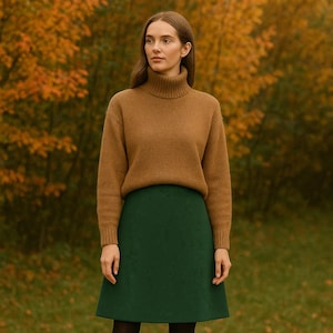 May include: A woman wearing a brown turtleneck sweater and a green skirt. The sweater is a solid color, and the skirt is a solid, dark green. The background features autumn foliage.