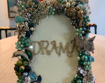 Espectacular marco de fotos vintage adornado con joyas, piezas únicas de turquesa, jade y plata con pedrería, alfileres y pendientes dispuestos de forma creativa. Tamaño: 8” x 6”.