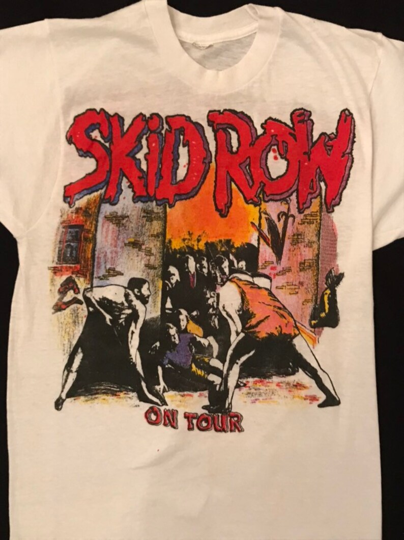 Op de afbeelding: Wit T-shirt met de bandnaam "SKID ROW" in rood en blauw, boven een afbeelding van een menigte. De tekst "ON TOUR" staat eronder in het rood. Het T-shirt is gemaakt van zacht, wit materiaal en is geschikt voor dagelijks gebruik.