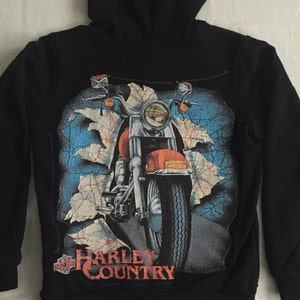 May include: Black zip-up hoodie with a Harley Davidson logo and a graphic of a motorcycle on the back. The graphic features a red motorcycle with a map background.