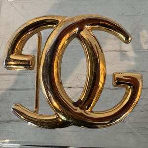 Puede incluir: Una hebilla de cinturón de metal dorado con un diseño de doble 'C'.