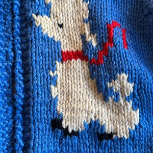 May include: A white knitted llama with a red ribbon around its neck is depicted on a blue knitted background.
