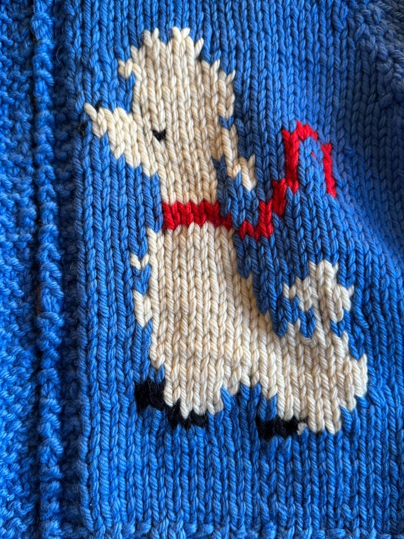 May include: A white knitted llama with a red ribbon around its neck is depicted on a blue knitted background.