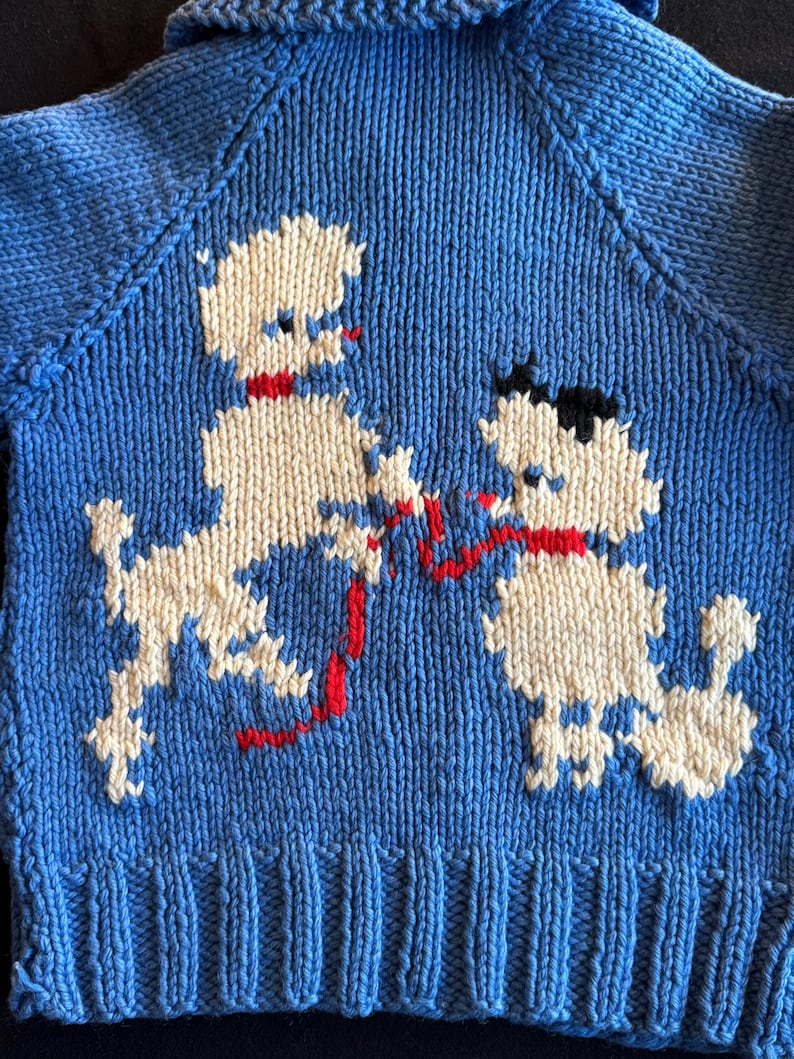 May include: A blue knitted sweater with a white and red poodle design. The sweater has a ribbed hem and a collar.