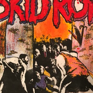 Op de afbeelding: Wit T-shirt met een grafisch ontwerp. De tekst "SKID ROW" is rood met een blauwe omlijning. De afbeelding toont een menigte mensen in een concertsetting, met de woorden "ON TOUR" onderaan.