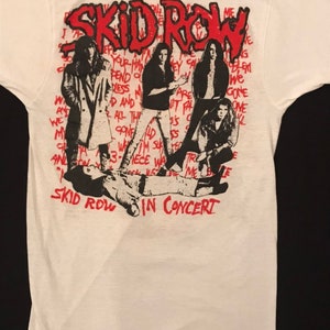 Op de afbeelding: Wit T-shirt met een afbeelding van de band Skid Row in concert. Het ontwerp bevat de naam van de band in het rood, bandleden en songteksten. Het shirt heeft een klassieke ronde hals en korte mouwen.