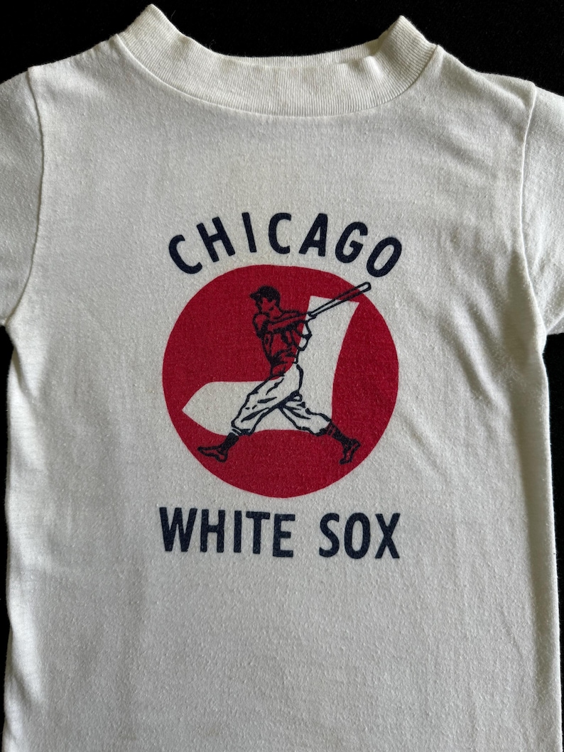 K&ouml;nnte beinhalten: Wei&szlig;es T-Shirt mit einem roten Kreis und einer Grafik eines Baseballspielers. Der Kreis tr&auml;gt den Text "CHICAGO" dar&uuml;ber und "WHITE SOX" darunter.