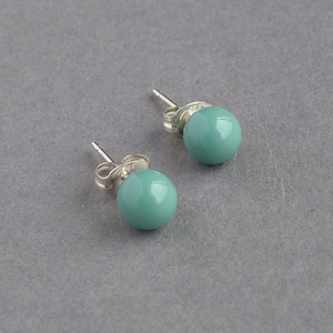 May include: A pair of silver stud earrings with teal round stones.