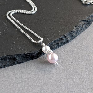 May include: A silver chain necklace with a pink and white pearl pendant. The pendant features a small rhinestone between the pearls.