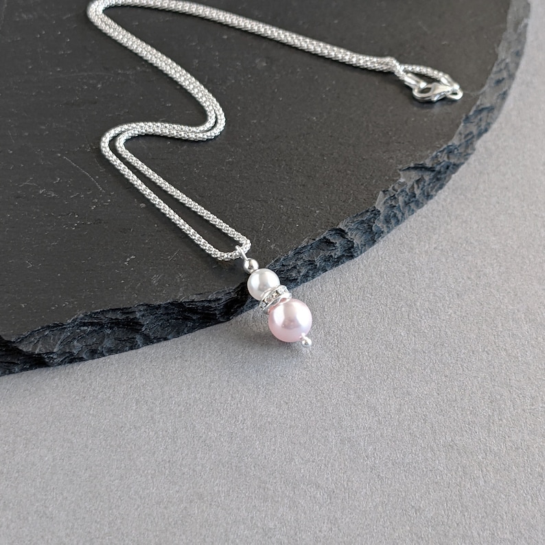 May include: A silver chain necklace with a pink and white pearl pendant. The pendant features a small rhinestone between the pearls.