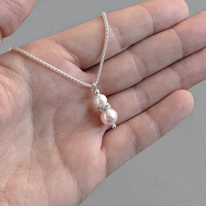 May include: A delicate silver chain necklace with a pink and white pearl pendant. The pendant features a small rhinestone accent.