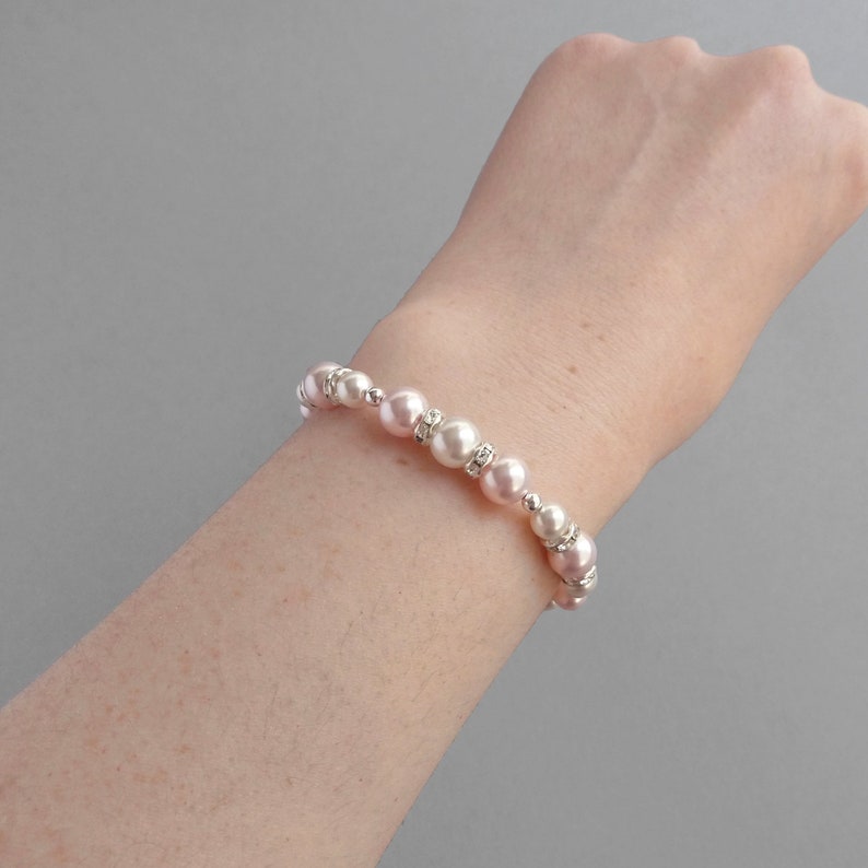 May include: A bracelet made of pink and white pearls with silver accents. The bracelet is on a person's wrist.