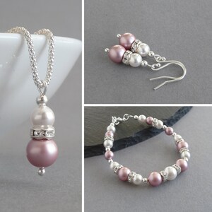 May include: A set of jewelry featuring a necklace, earrings, and a bracelet. The jewelry is made with silver and pink and white pearls. The necklace has a pendant with a pink pearl and a white pearl. The earrings have a pink pearl and a white pearl. The bracelet has alternating pink and white pearls.