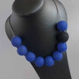 May include: A necklace made of blue and black felt balls. The necklace is on a black mannequin bust.