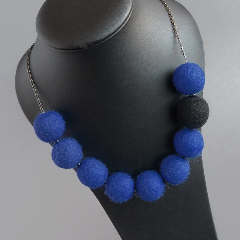 May include: A necklace made of blue and black felt balls. The necklace is on a black mannequin bust.