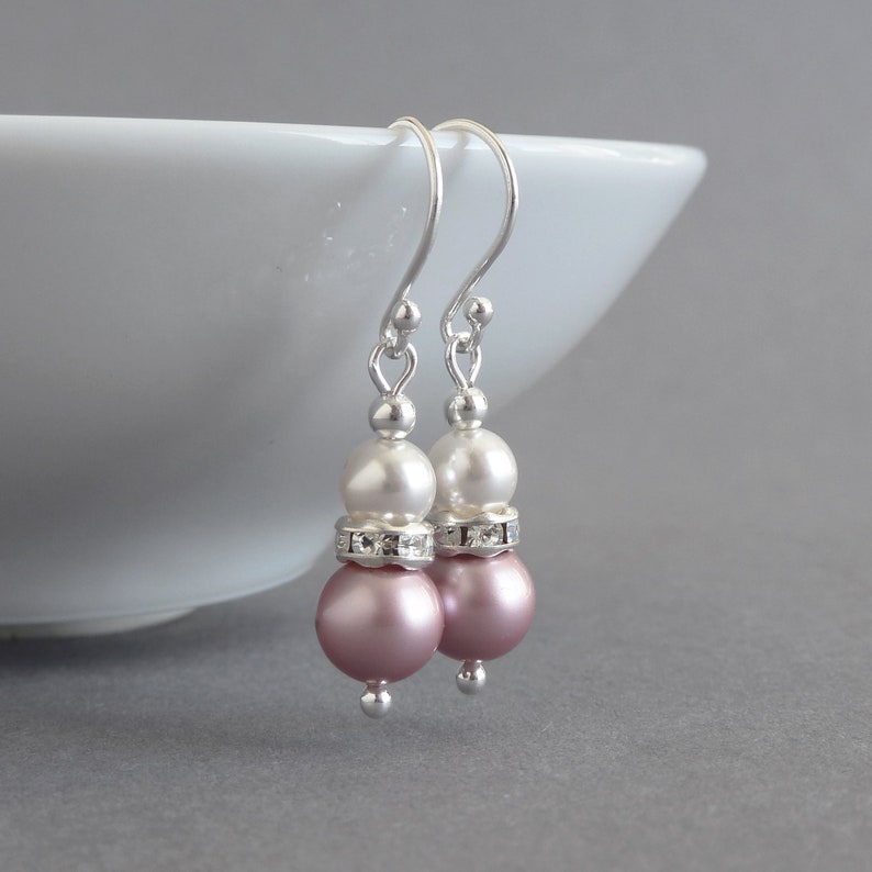 May include: A pair of silver dangle earrings with two white pearls and a pink pearl on each earring. The pearls are separated by a silver band of rhinestones.