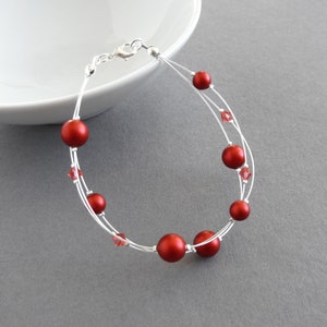 May include: A silver bracelet with red beads and clear crystals. The bracelet is made of thin wire and has a delicate look.