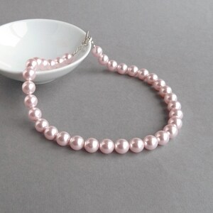 May include: A delicate pink pearl necklace with a silver clasp. The pearls are evenly spaced and create a classic and elegant look.