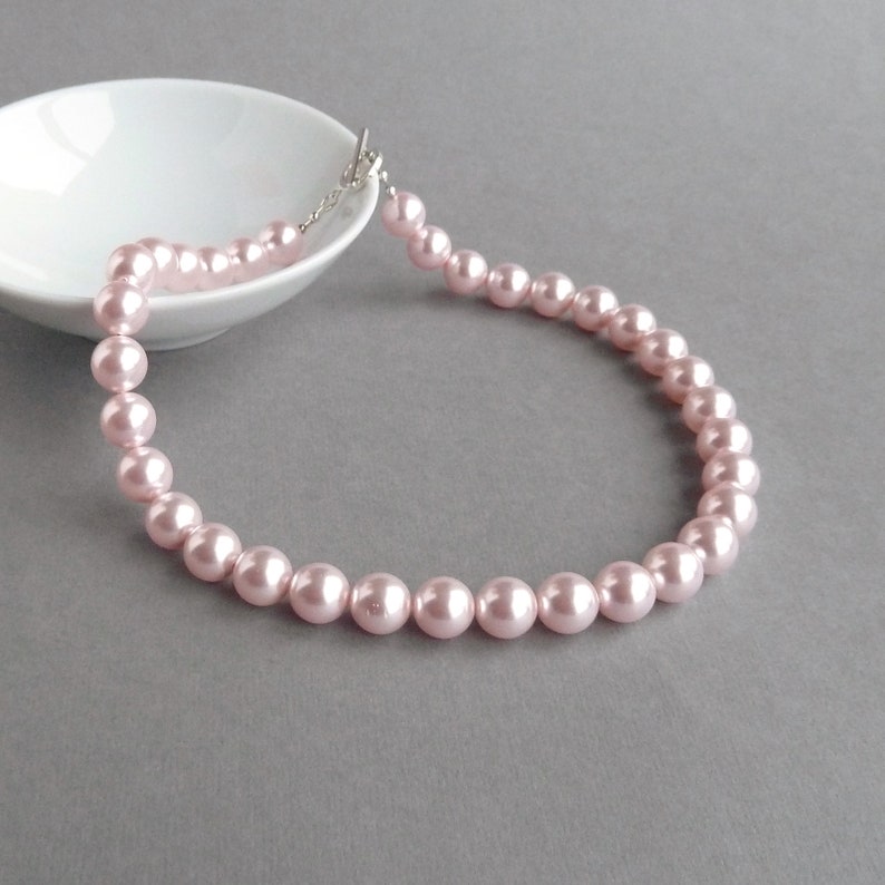 May include: A delicate pink pearl necklace with a silver clasp. The pearls are evenly spaced and create a classic and elegant look.